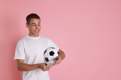 Happy man with money and soccer ball on pink background, space for text