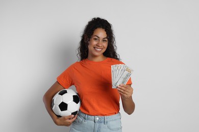 Happy woman with money and soccer ball on light grey background