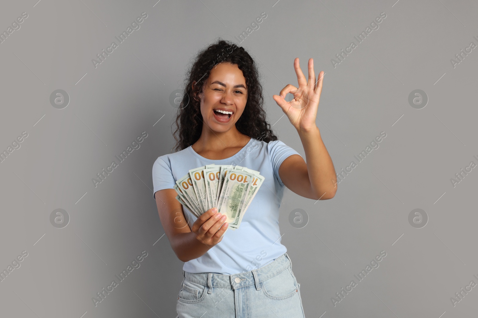 Photo of Happy woman with dollar banknotes showing ok gesture on grey background