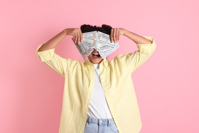 Woman covering eyes with dollar banknotes on pink background