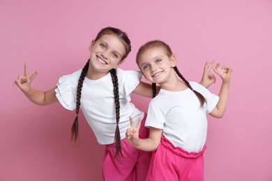 Portrait of cute little sisters on pink background