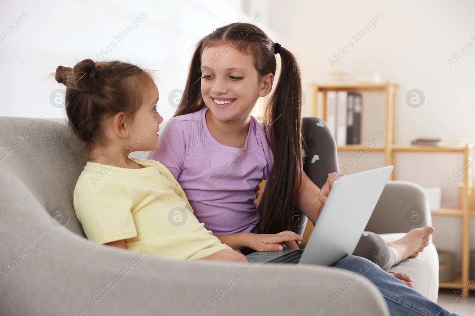 Photo of Cute little sisters with laptop spending time together at home