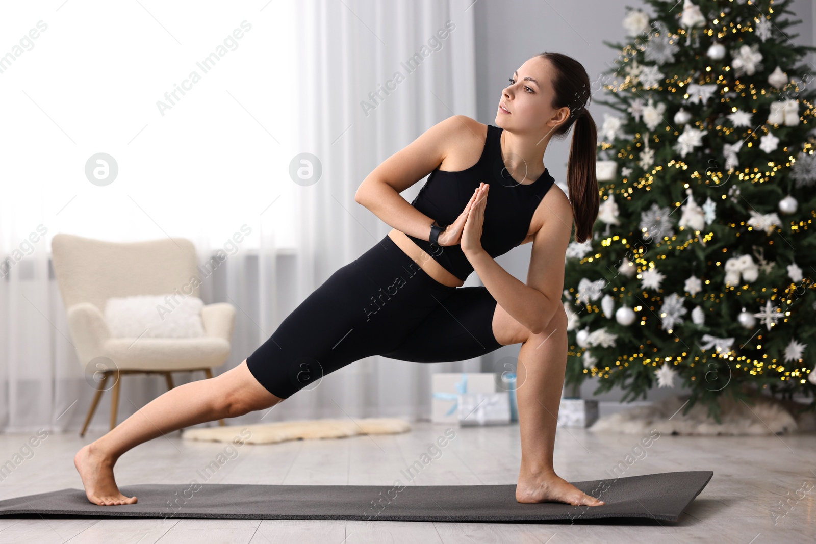 Photo of Woman practicing yoga against Christmas tree indoors