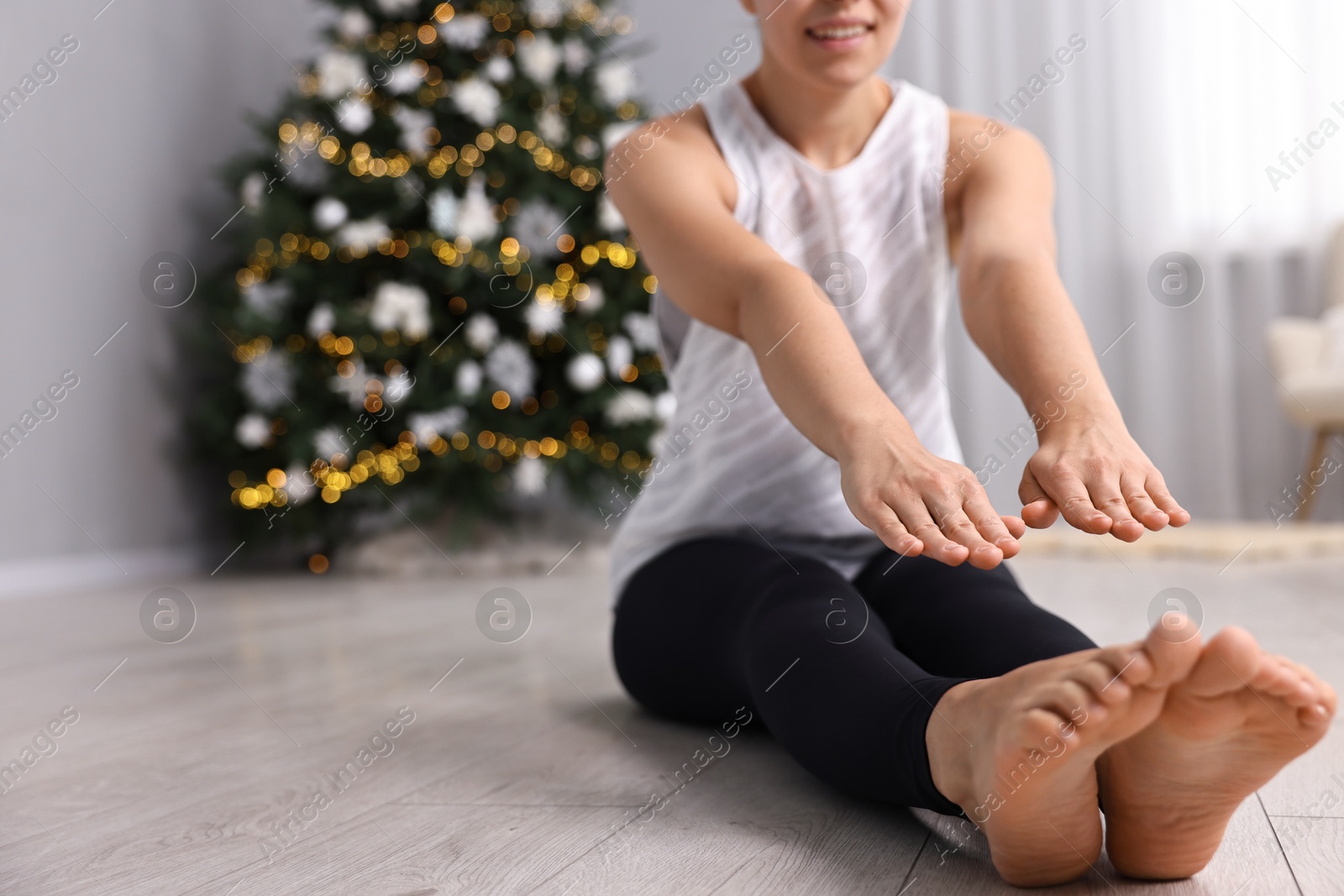 Photo of Woman practicing yoga against blurred Christmas lights indoors, closeup