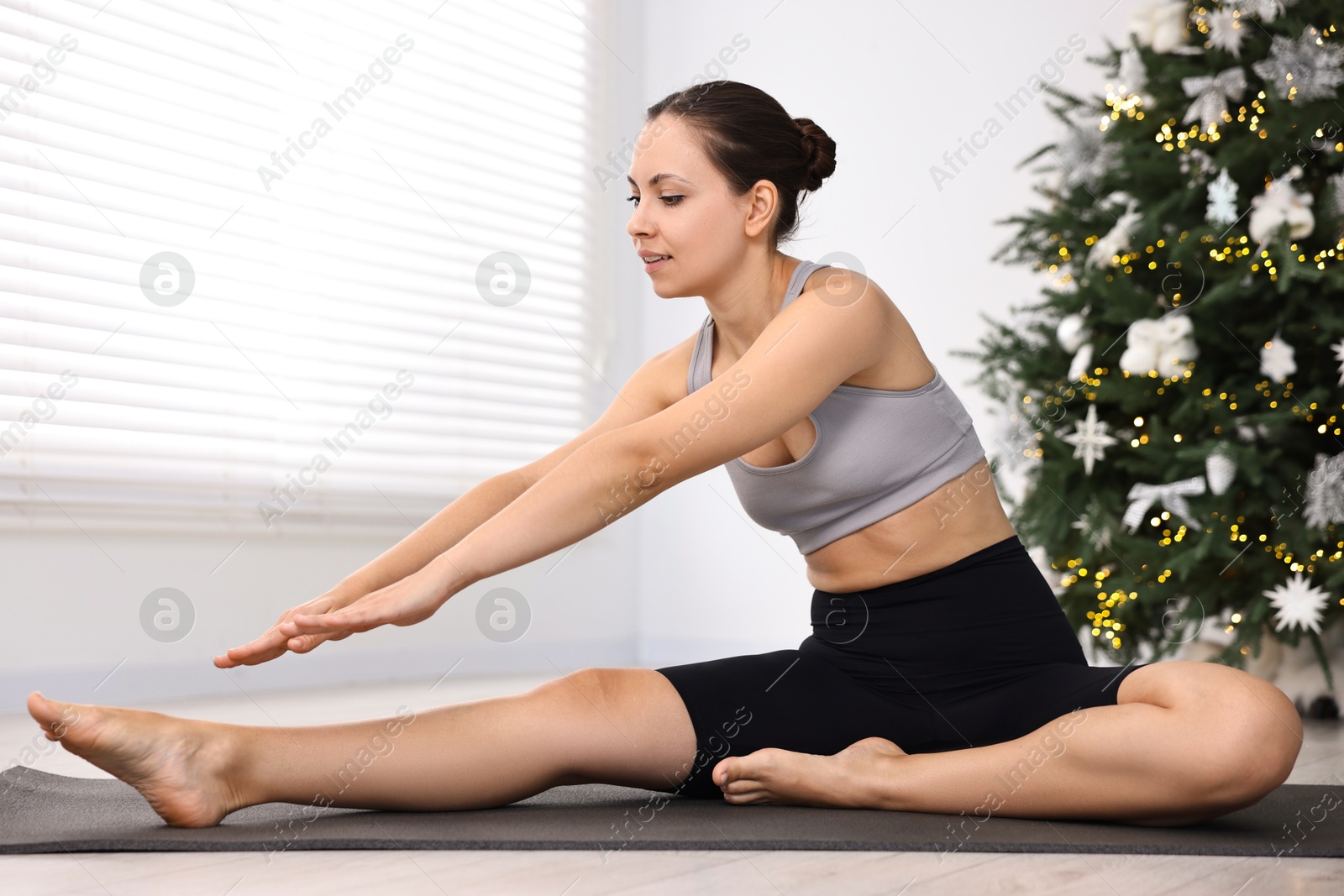 Photo of Woman practicing yoga against Christmas tree indoors