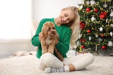 Woman with cute Maltipoo dog on rug in room decorated for Christmas