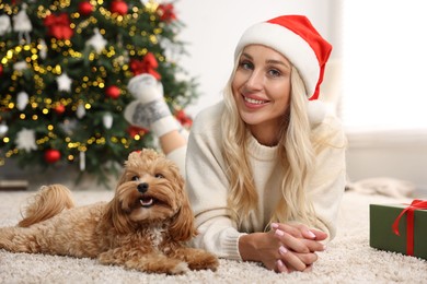 Photo of Woman with cute Maltipoo dog on rug in room decorated for Christmas