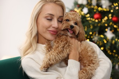 Photo of Woman with cute Maltipoo dog in room decorated for Christmas