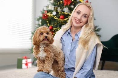 Photo of Woman with cute Maltipoo dog on floor in room decorated for Christmas