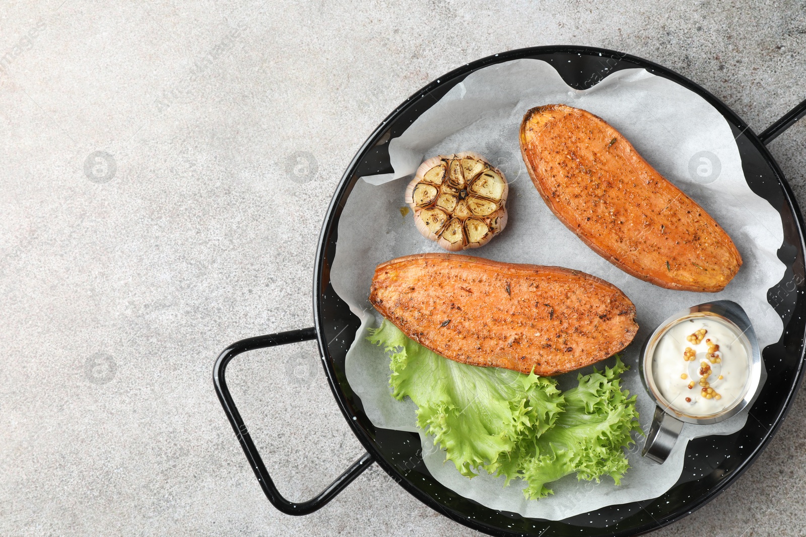 Photo of Tasty cooked sweet potato served in baking dish on grey textured table, top view. Space for text