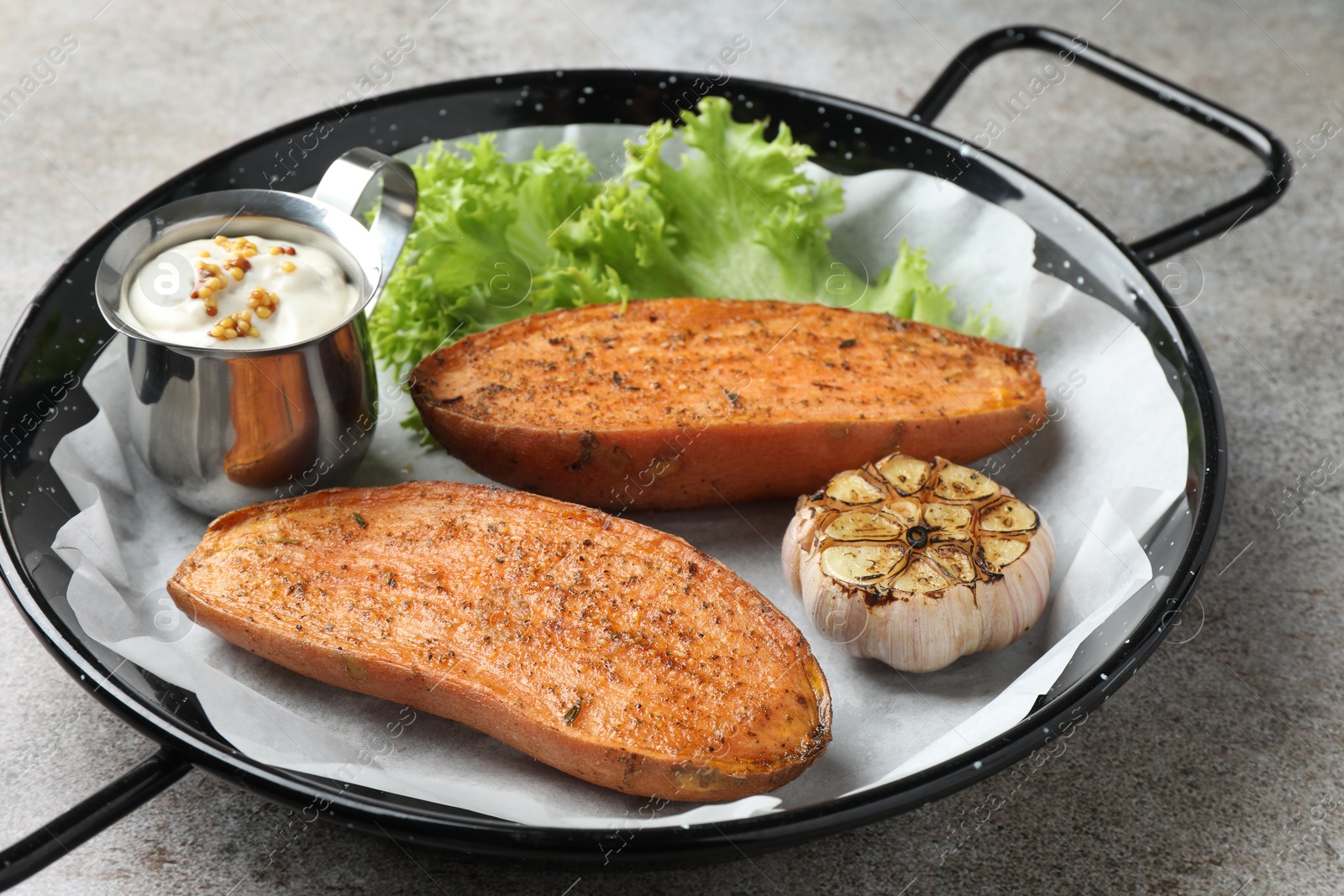 Photo of Tasty cooked sweet potato served in baking dish on grey textured table, closeup