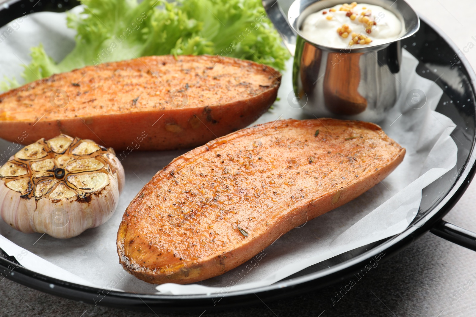 Photo of Tasty cooked sweet potato served in baking dish on grey table, closeup