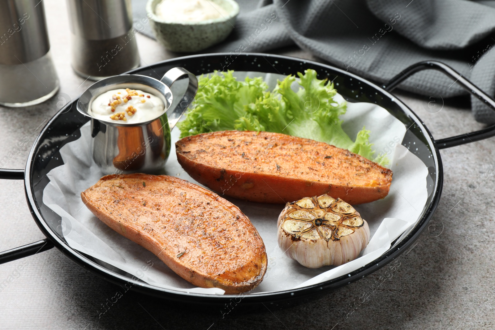 Photo of Tasty cooked sweet potato in baking dish served on grey textured table