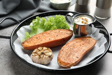 Photo of Tasty cooked sweet potato in baking dish served on grey textured table, closeup