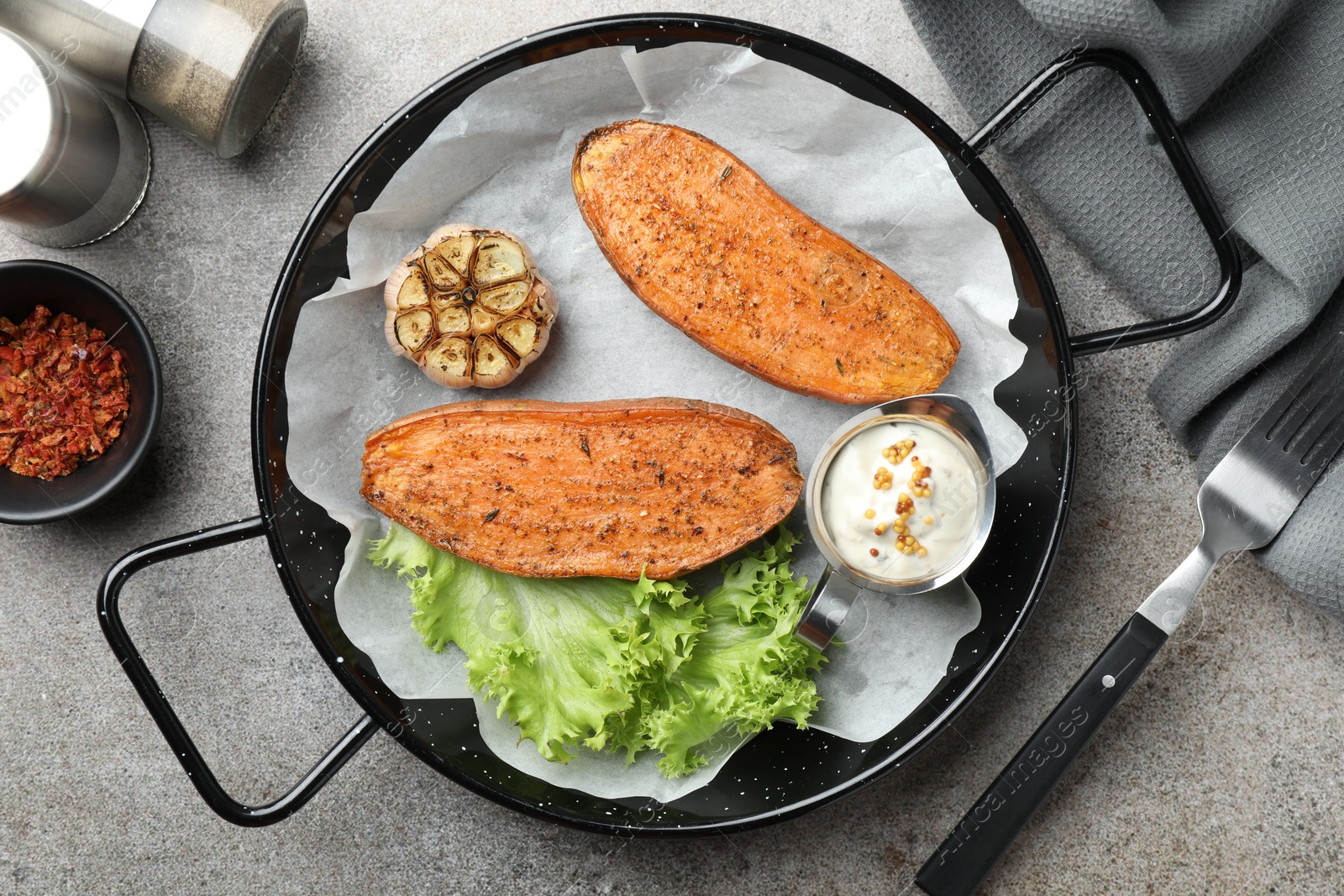 Photo of Tasty cooked sweet potato in baking dish served on grey textured table, flat lay