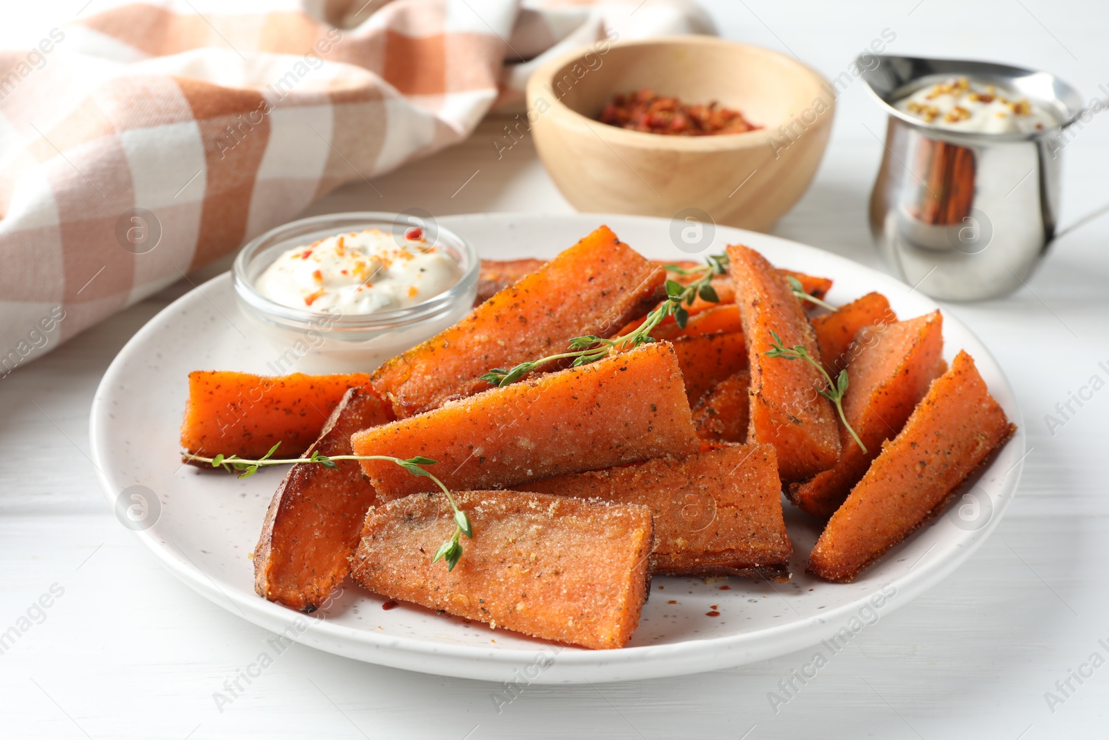 Photo of Pieces of tasty baked sweet potato with microgreens served on white wooden table, closeup