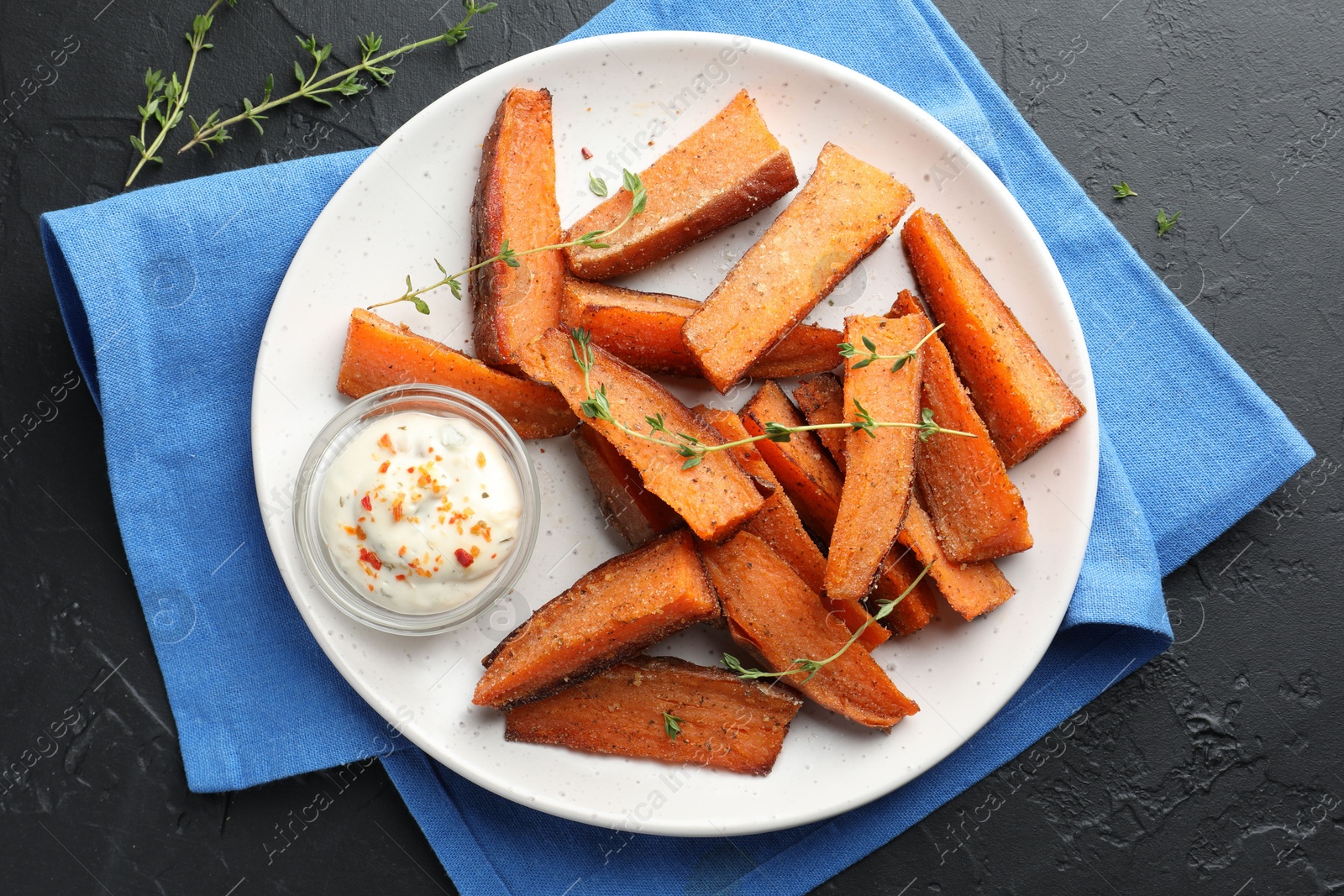 Photo of Pieces of tasty baked sweet potato with microgreens and sauce on grey textured table, flat lay