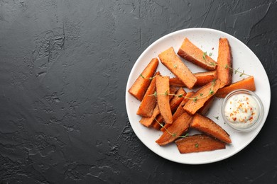 Photo of Pieces of tasty baked sweet potato with microgreens and sauce on grey textured table, top view