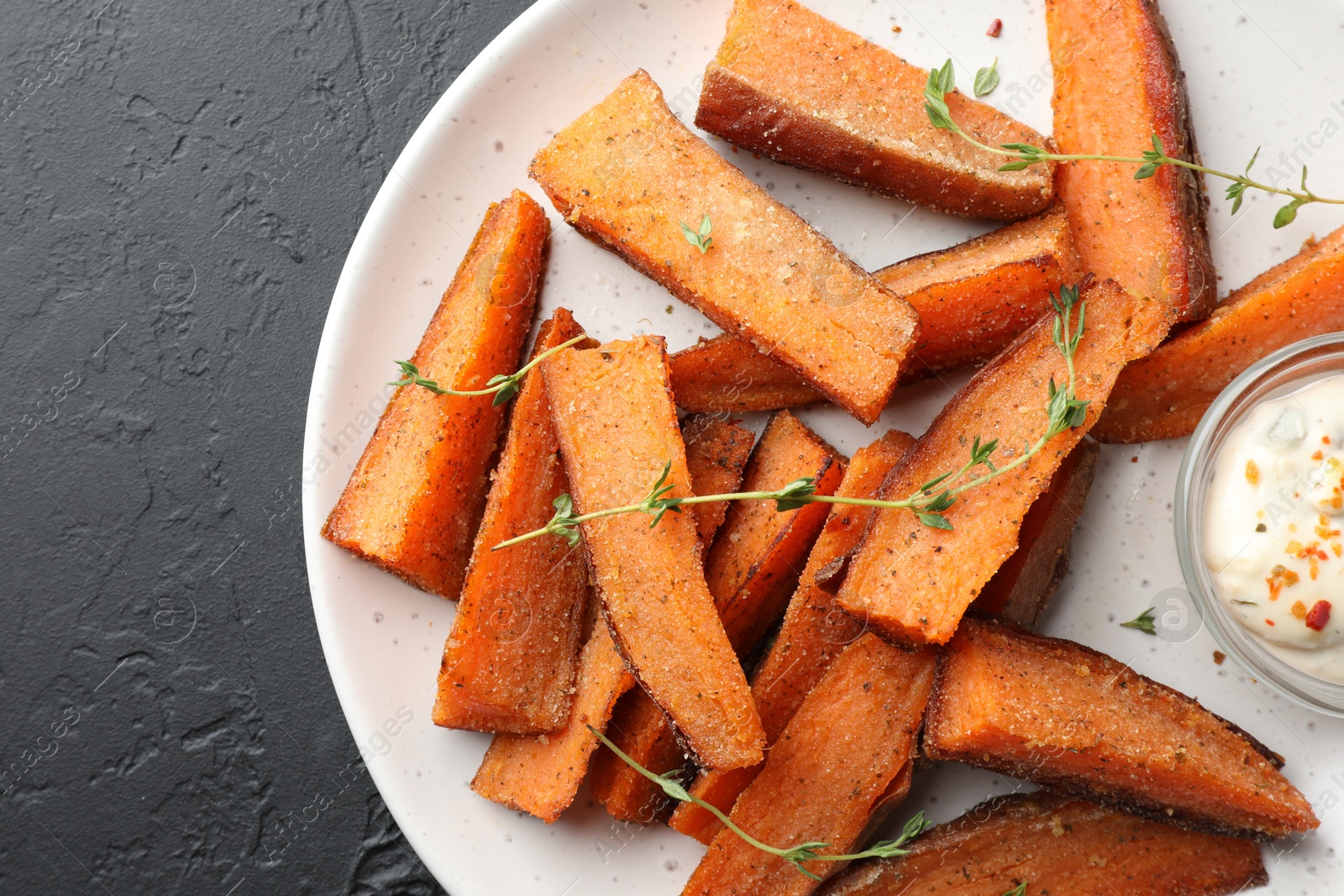 Photo of Pieces of tasty baked sweet potato with microgreens and sauce on grey textured table, flat lay