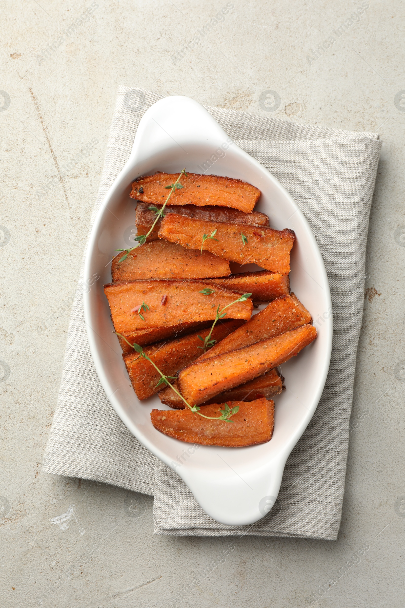 Photo of Pieces of tasty cooked sweet potato with microgreens in baking dish on light textured table, top view