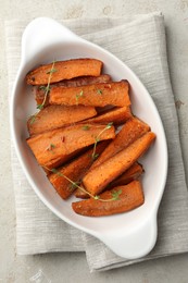 Photo of Pieces of tasty cooked sweet potato with microgreens in baking dish on light textured table, top view