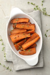 Photo of Pieces of tasty cooked sweet potato in baking dish with microgreens on light textured table, top view