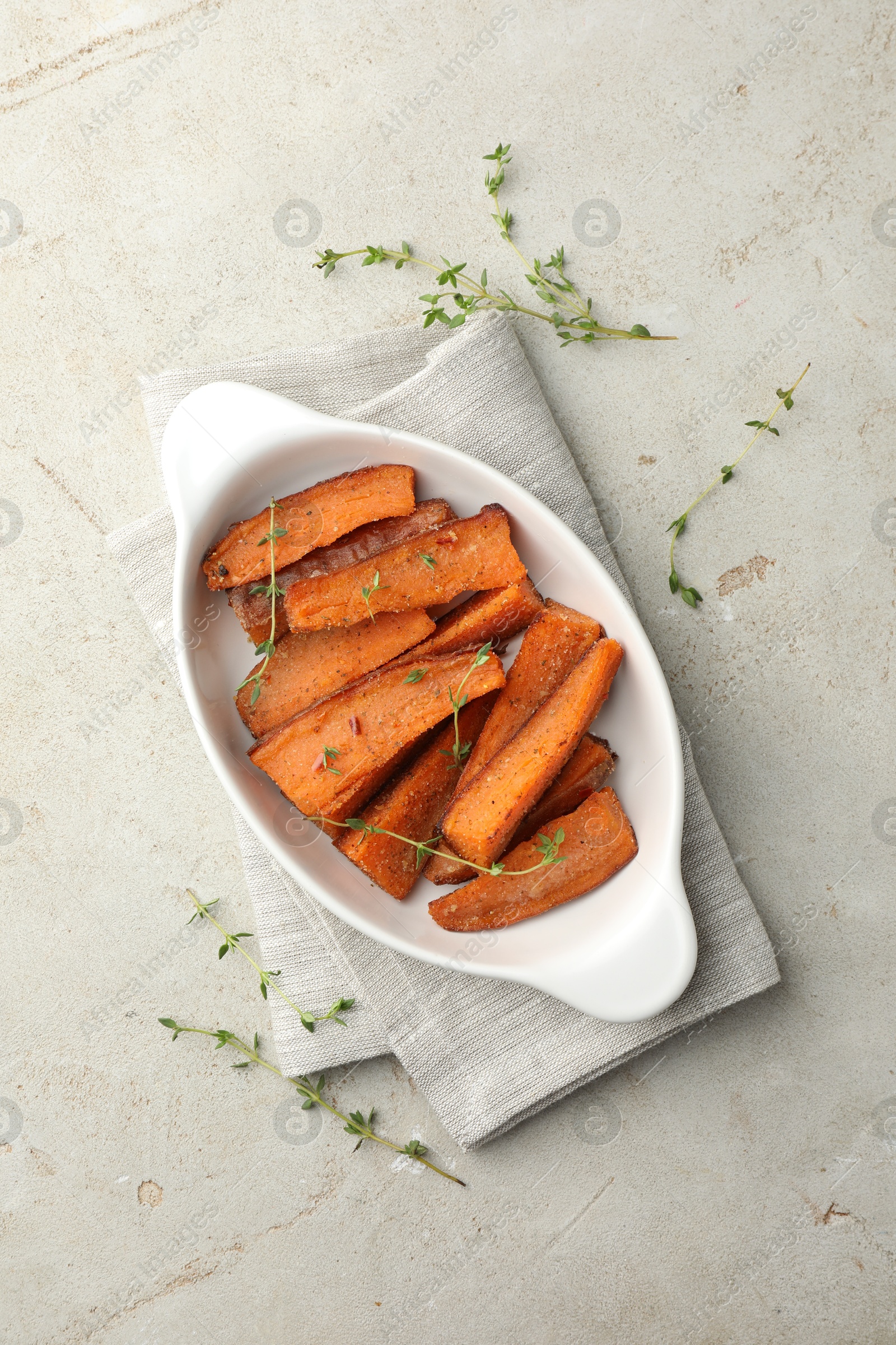 Photo of Pieces of tasty cooked sweet potato in baking dish with microgreens on light textured table, top view