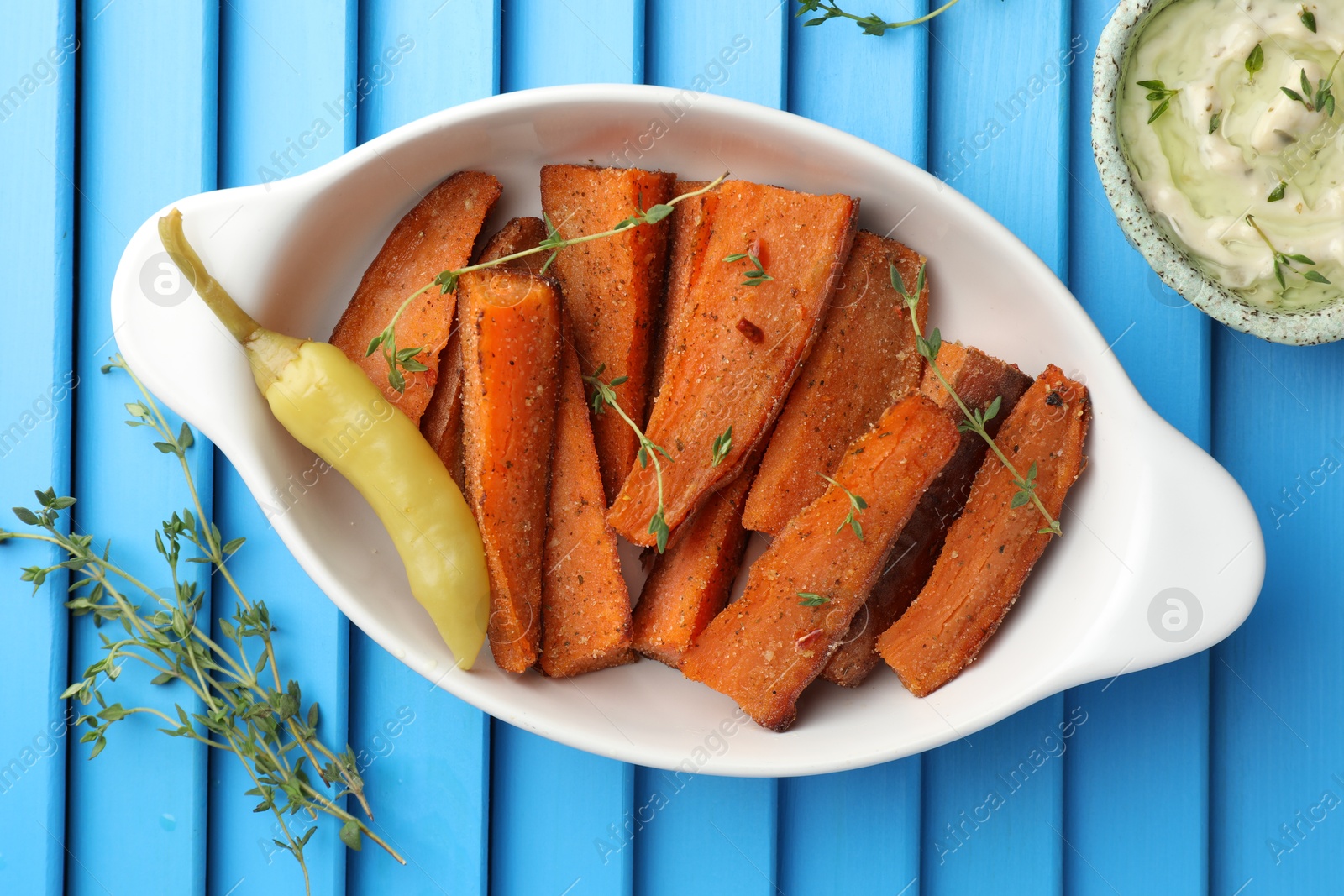 Photo of Pieces of tasty cooked sweet potato in baking dish served on blue textured table, flat lay