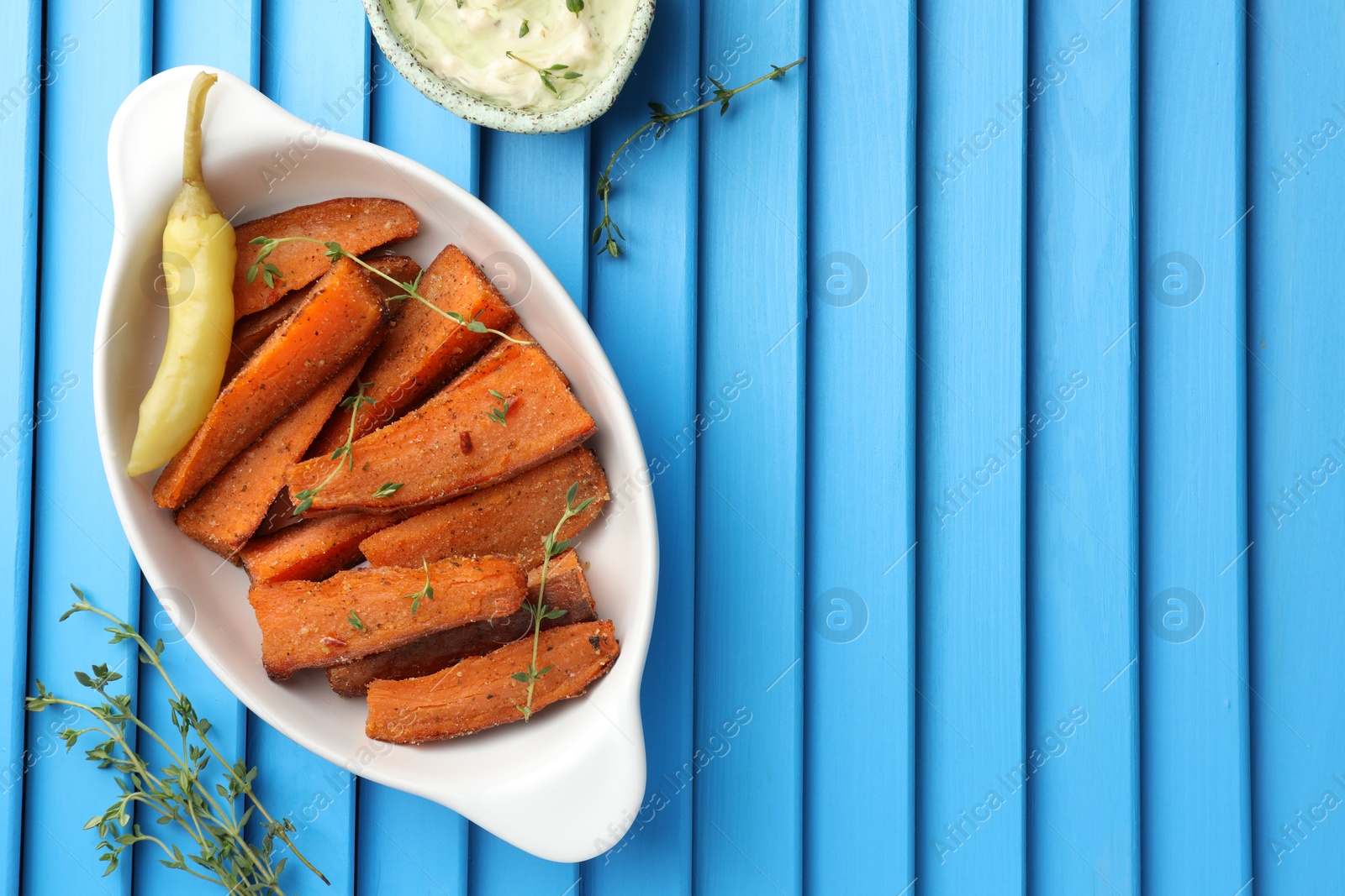 Photo of Pieces of tasty cooked sweet potato in baking dish served on blue textured table, flat lay. Space for text