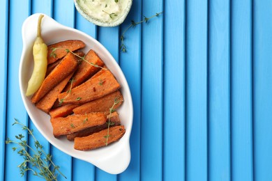 Pieces of tasty cooked sweet potato in baking dish served on blue textured table, flat lay. Space for text