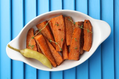 Photo of Pieces of tasty cooked sweet potato with microgreens and bell pepper in baking dish on blue textured table, top view