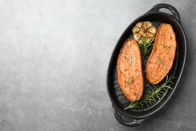 Halves of tasty cooked sweet potato with rosemary and garlic in baking dish on grey textured table, top view. Space for text