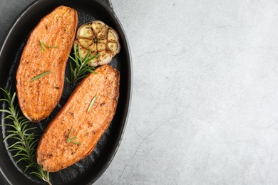 Photo of Halves of tasty cooked sweet potato with rosemary and garlic in baking dish on grey textured table, top view. Space for text