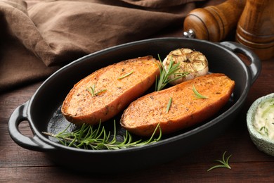 Photo of Halves of tasty cooked sweet potato in baking dish served on wooden table