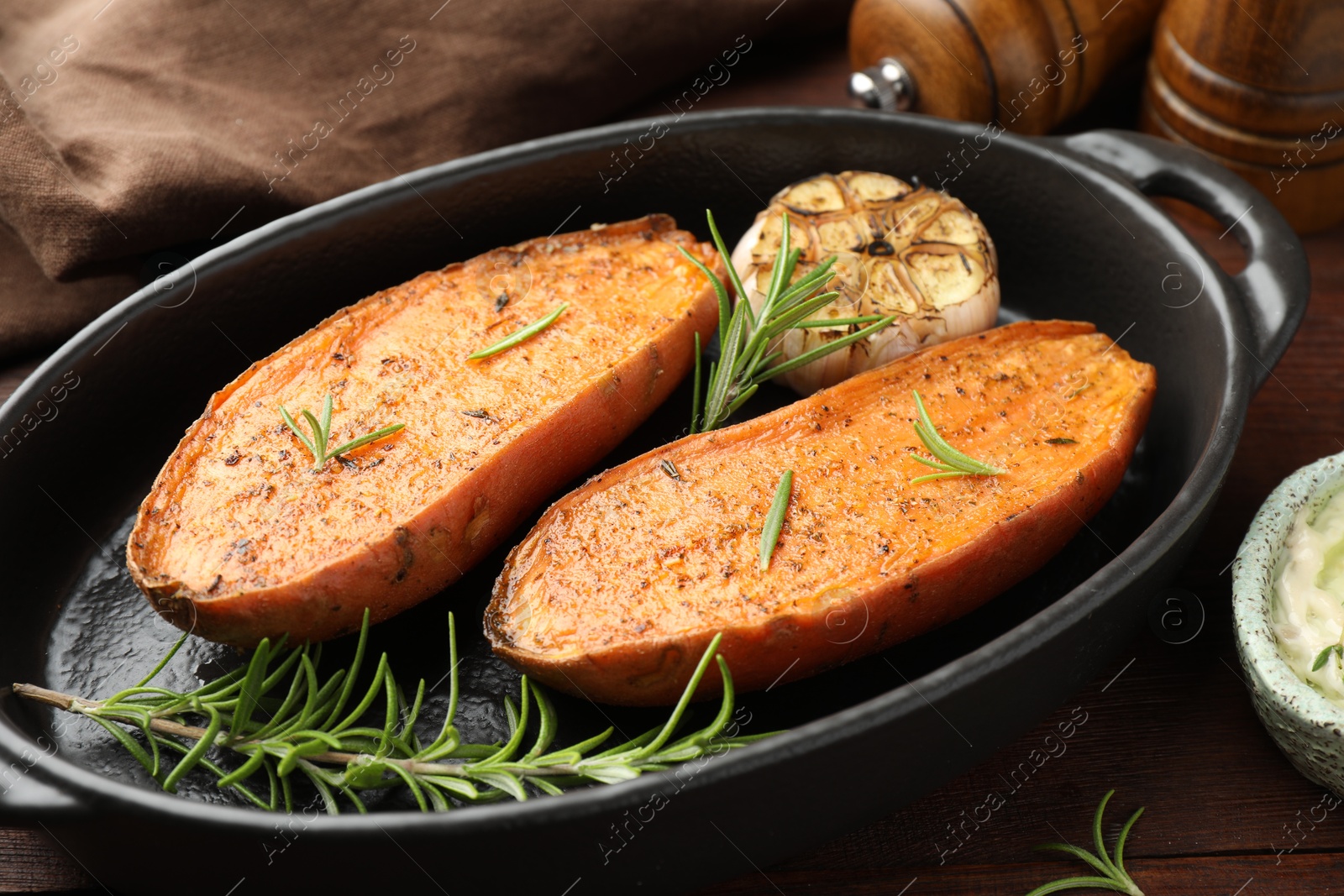 Photo of Halves of tasty cooked sweet potato in baking dish served on wooden table, closeup