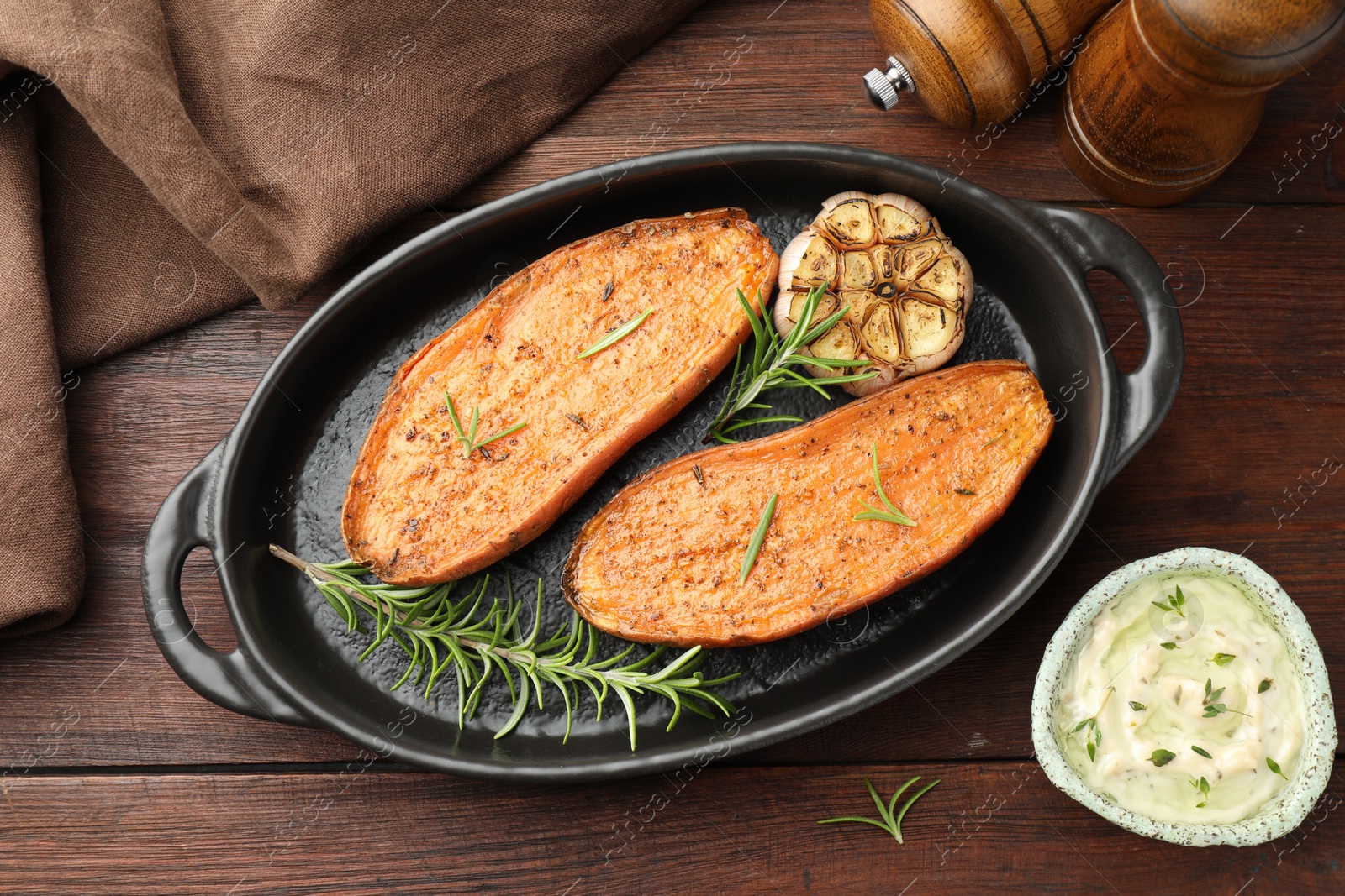 Photo of Halves of tasty cooked sweet potato in baking dish served on wooden table, flat lay