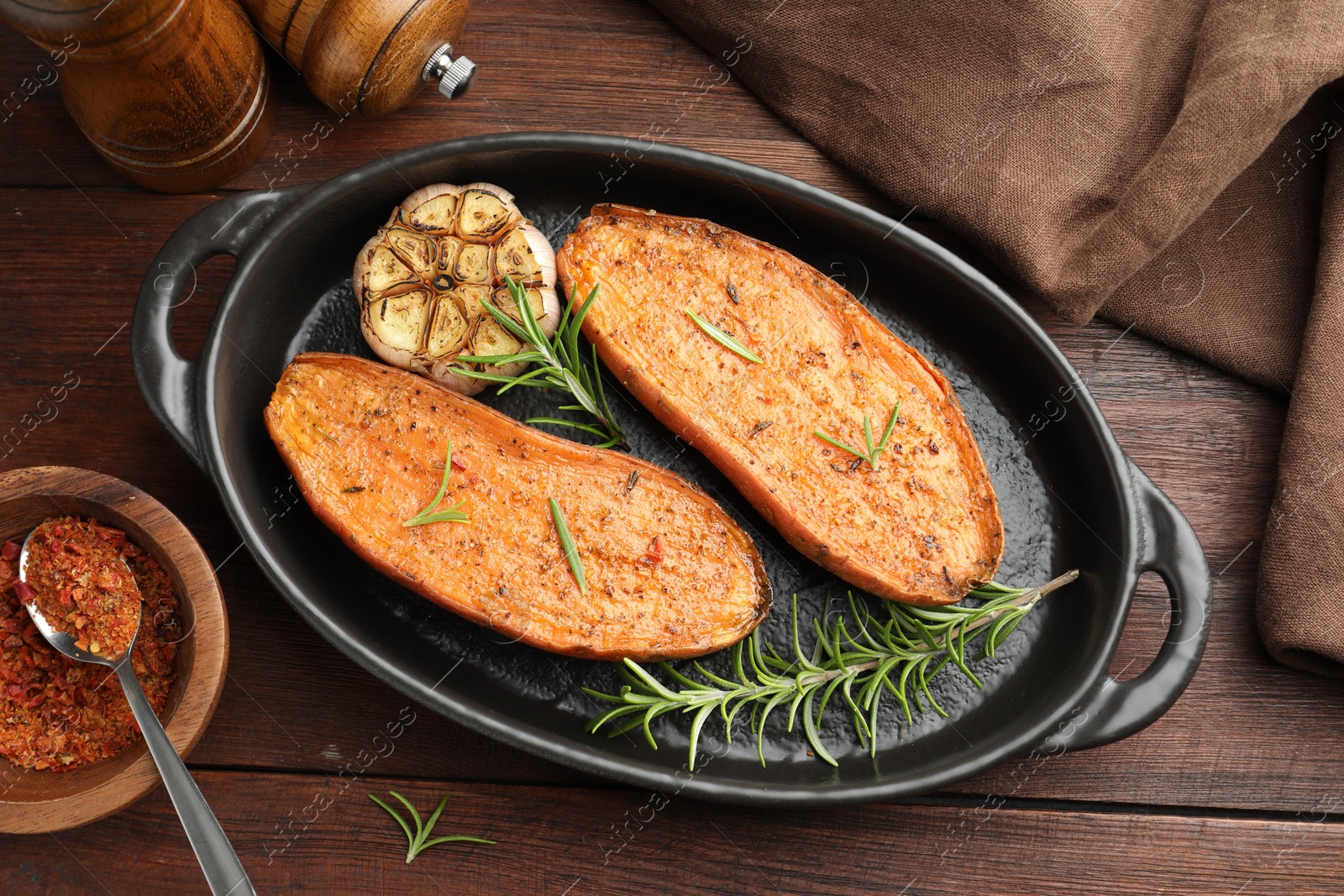 Photo of Halves of tasty cooked sweet potato in baking dish served on wooden table, flat lay