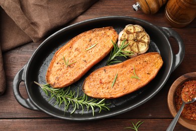 Photo of Halves of tasty cooked sweet potato in baking dish served on wooden table, flat lay