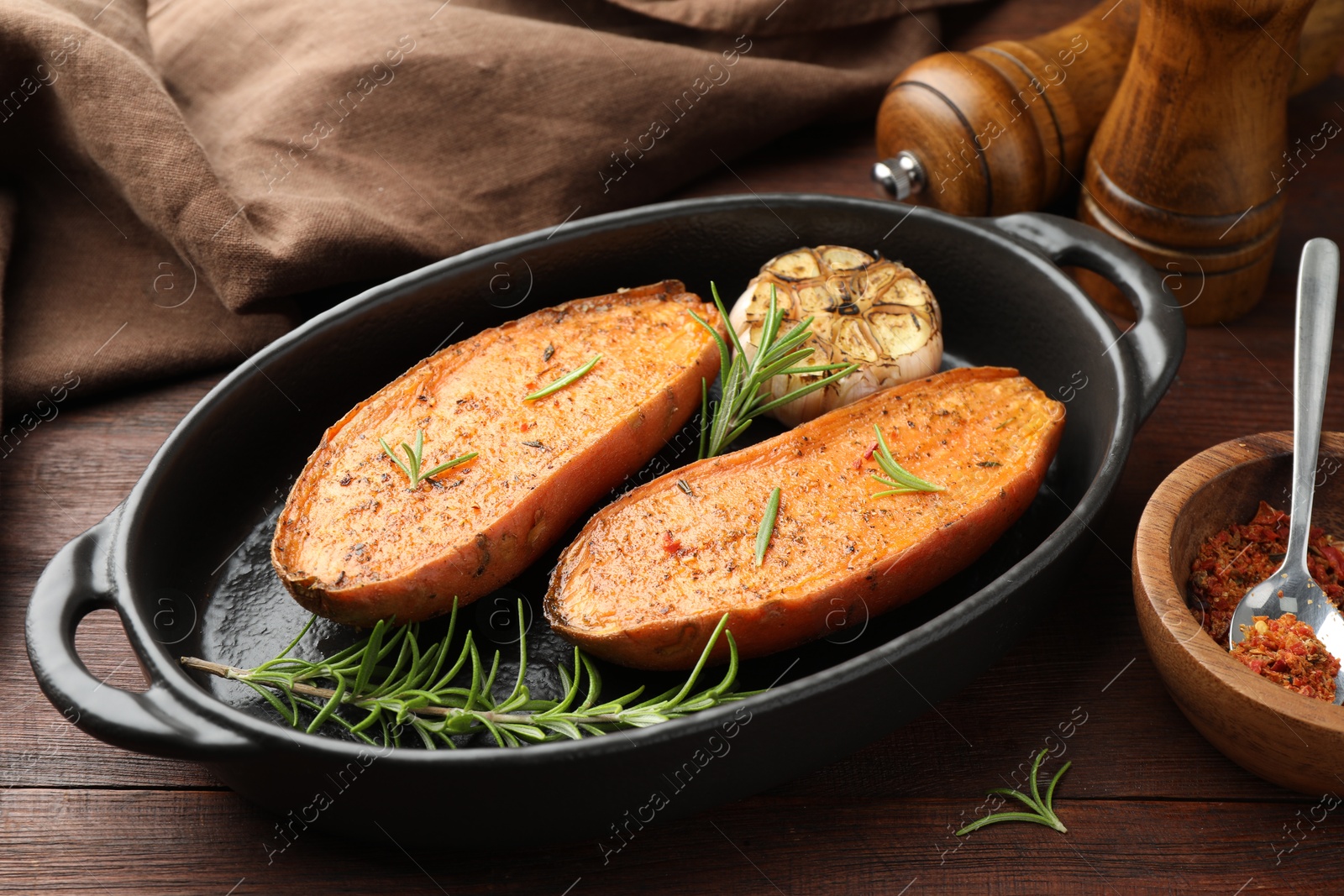 Photo of Halves of tasty cooked sweet potato in baking dish served on wooden table