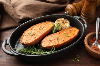 Halves of tasty cooked sweet potato in baking dish served on wooden table