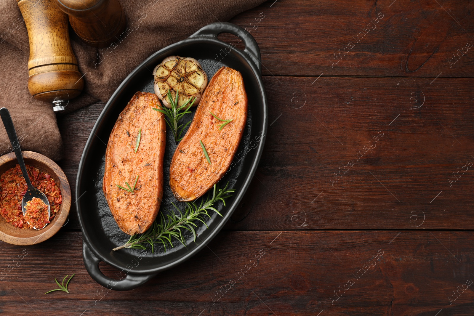 Photo of Halves of tasty cooked sweet potato in baking dish served on wooden table, flat lay. Space for text