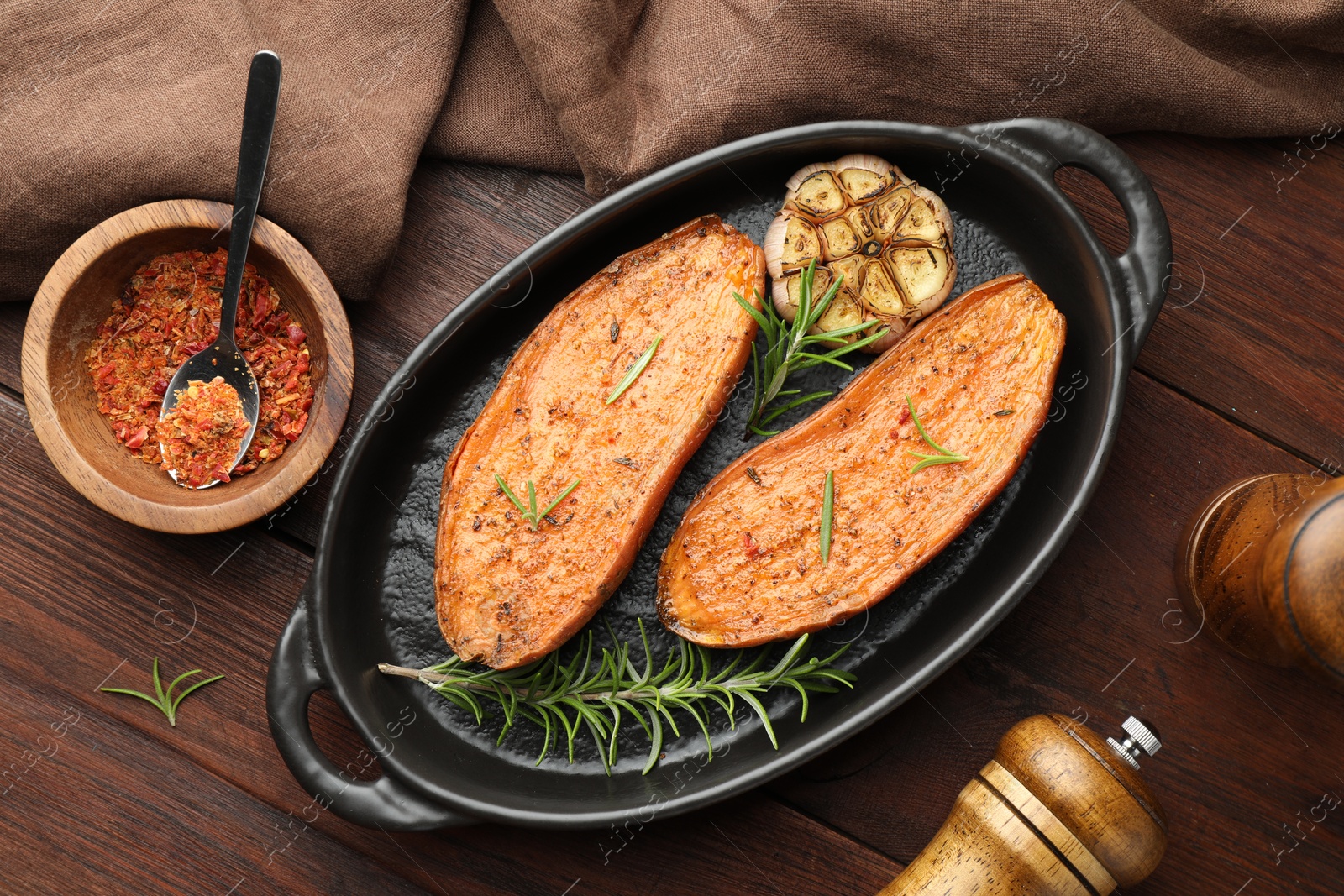 Photo of Halves of tasty cooked sweet potato in baking dish served on wooden table, flat lay