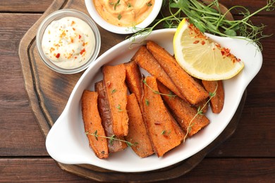 Photo of Pieces of tasty cooked sweet potato in baking dish served on wooden table, top view