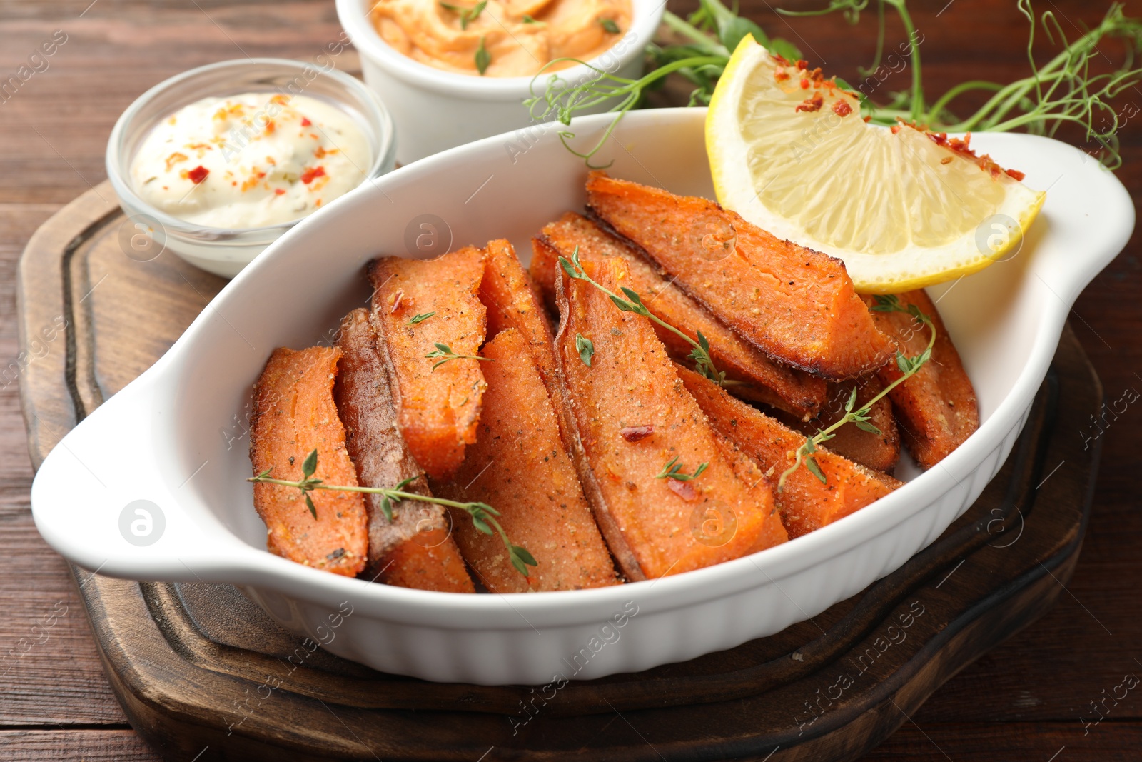 Photo of Pieces of tasty cooked sweet potato in baking dish served on wooden table, closeup