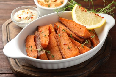 Photo of Pieces of tasty cooked sweet potato in baking dish served on wooden table, closeup