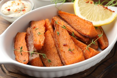 Photo of Pieces of tasty cooked sweet potato in baking dish served on wooden table, closeup