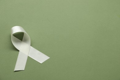 Photo of White awareness ribbon on green background, top view. Space for text