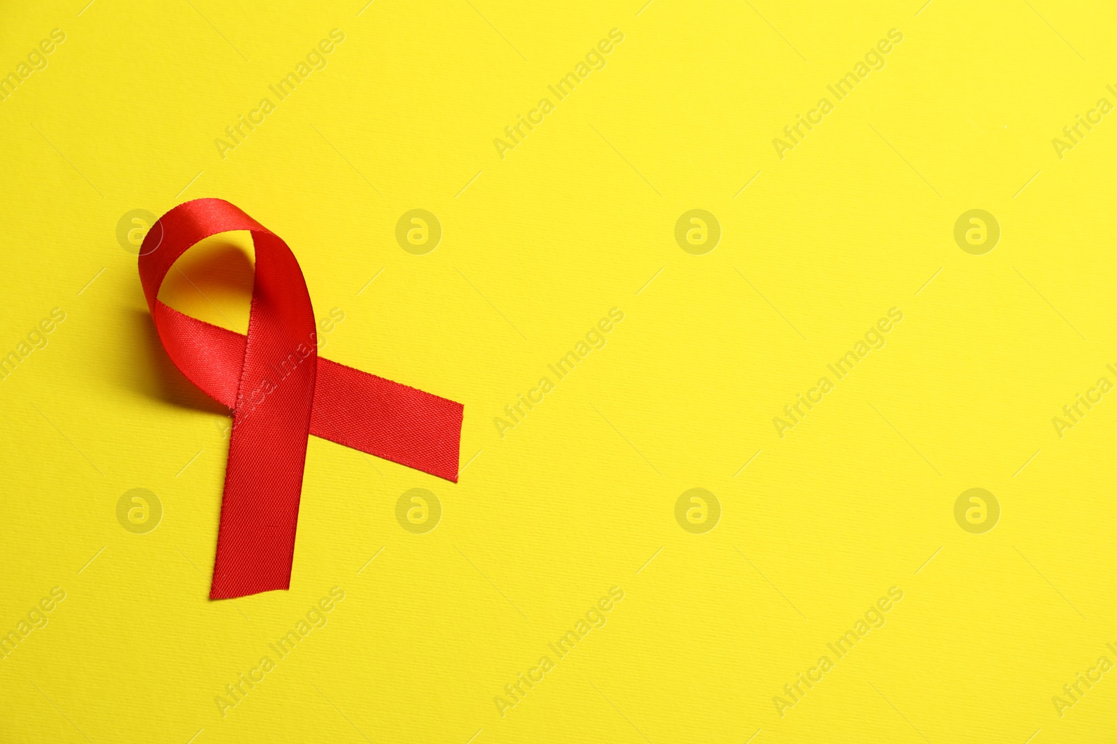 Photo of Red awareness ribbon on yellow background, top view. Space for text