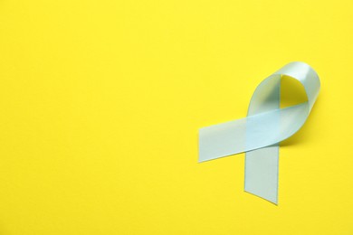 Photo of Light blue awareness ribbon on yellow background, top view. Space for text