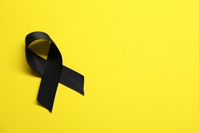 Black awareness ribbon on yellow background, top view. Space for text